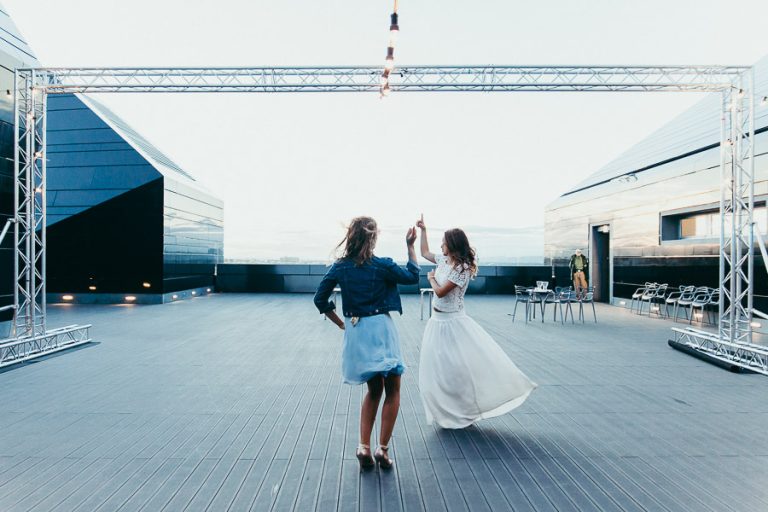 Novia y amiga bailando bajo estructura y guirnaldas