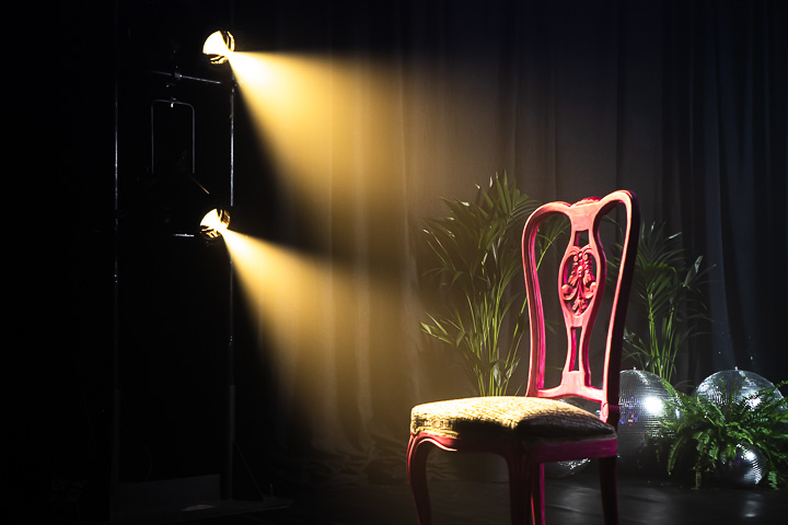 Focos en calle de teatro iluminando una silla rosa